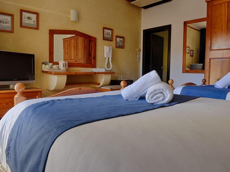 Gezellige hotelkamer met tweepersoonsbed, blauwe deken, houten meubels en warm licht.