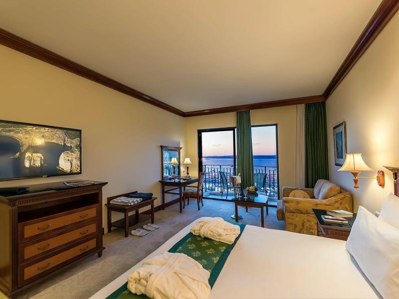 Moderne hotelkamer met tweepersoonsbed, tv, zithoek en balkon met zeezicht