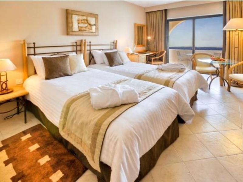 Helles Hotelzimmer mit zwei Betten, braun-beigen Möbeln und großem Fenster mit Aussicht.