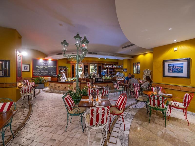 Gemütlicher Barbereich mit roten gestreiften Stühlen, gelben Wänden und Pflastersteinboden.