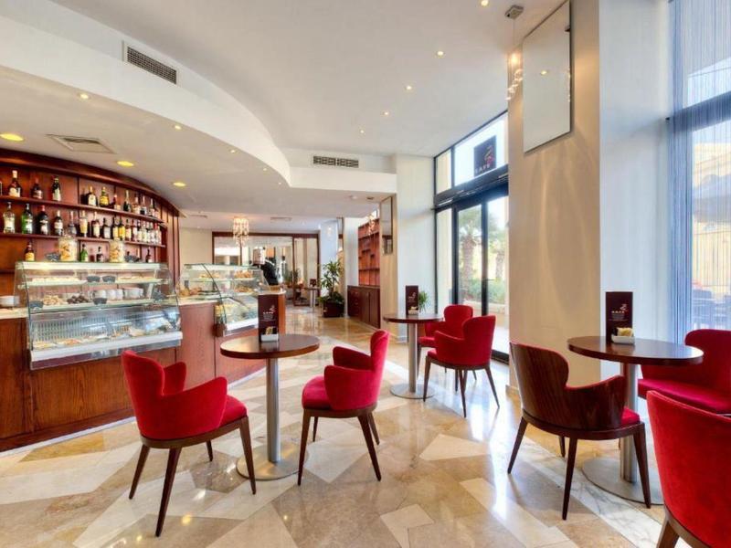 Modernes Café mit großen Fenstern, roten Stühlen, marmornem Boden und einer Theke voller Getränke.