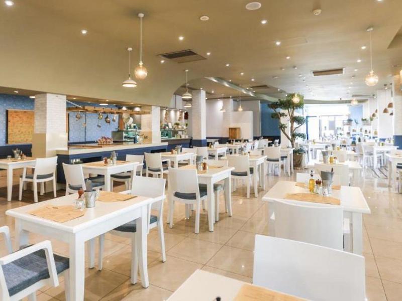 Großer, heller Speisesaal mit weißen Tischen, Stühlen und moderner Beleuchtung.