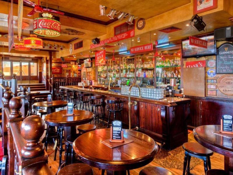 Gemütliche Bar mit dunklem Holz, runden Tischen, Hockern und warmem Licht.