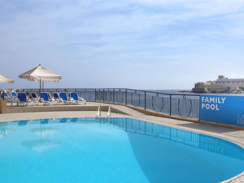 Großer Außenpool mit blauer Wasserfläche, Liegestühlen, Schirmen und Blick auf das Meer.