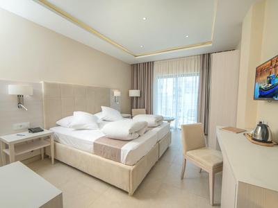 Helles Hotelzimmer mit großem Doppelbett, Schreibtisch, Stuhl und Balkon mit Vorhängen.