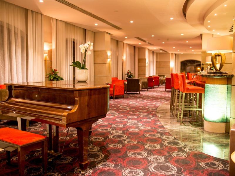 Luxury hotel lounge with grand piano, red chairs, and patterned carpet under warm lighting.