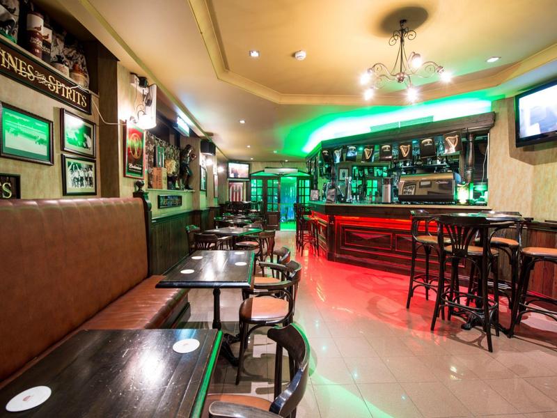 Cozy hotel bar with wooden tables, chairs, brown sofa, and neon-lit counter.