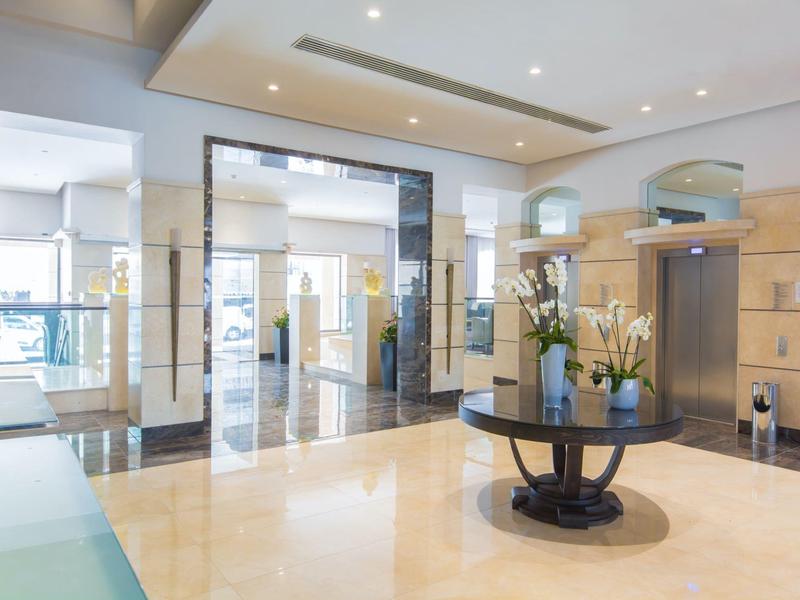 Bright hotel lobby with polished floor, central round table with flowers, and glass doors.