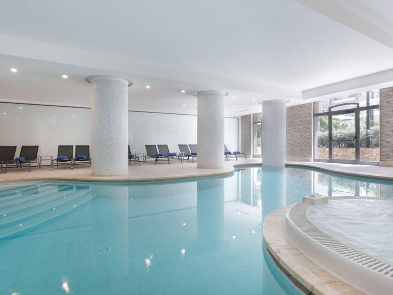 Indoor pool with lounge chairs and large windows letting in natural light.