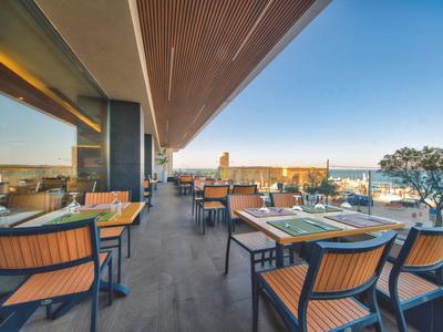 Moderner Außenbereich eines Restaurants mit Meerblick und gedeckten Tischen.