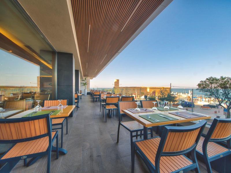 Moderner Außenbereich eines Restaurants mit Holzstühlen und Blick auf das Meer.