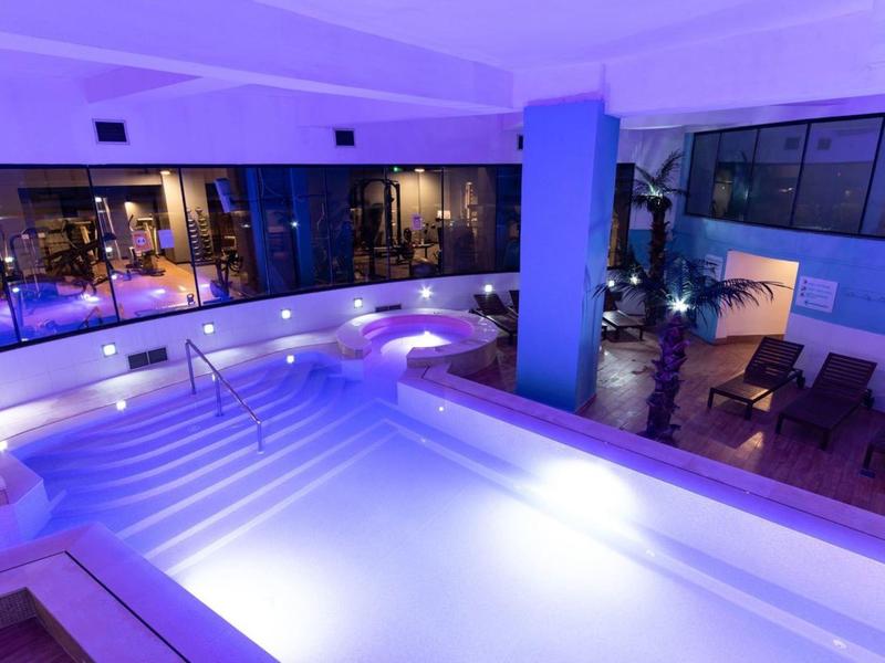 Moderner Indoor-Pool in einem Hotel mit blauer Beleuchtung und Liegestühlen.