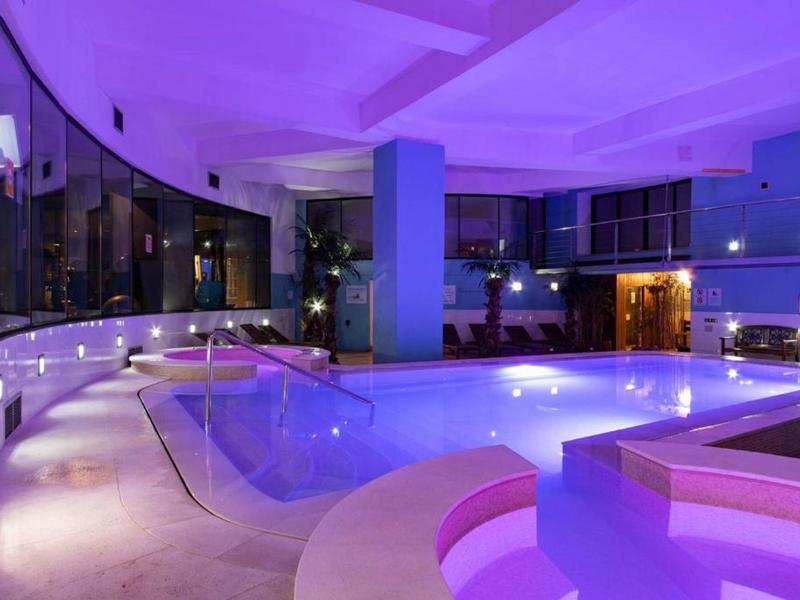 Modernes Schwimmbad in einem Hotel mit lila Beleuchtung bei Nacht.