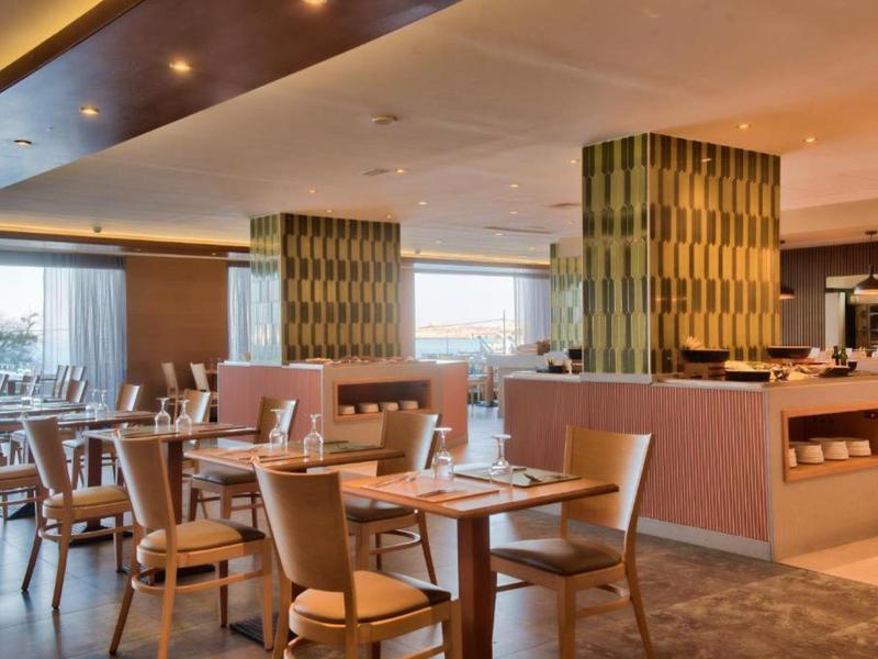 Moderner Hotelrestaurantbereich mit Holztischen, bequemen Stühlen und großen Fenstern.