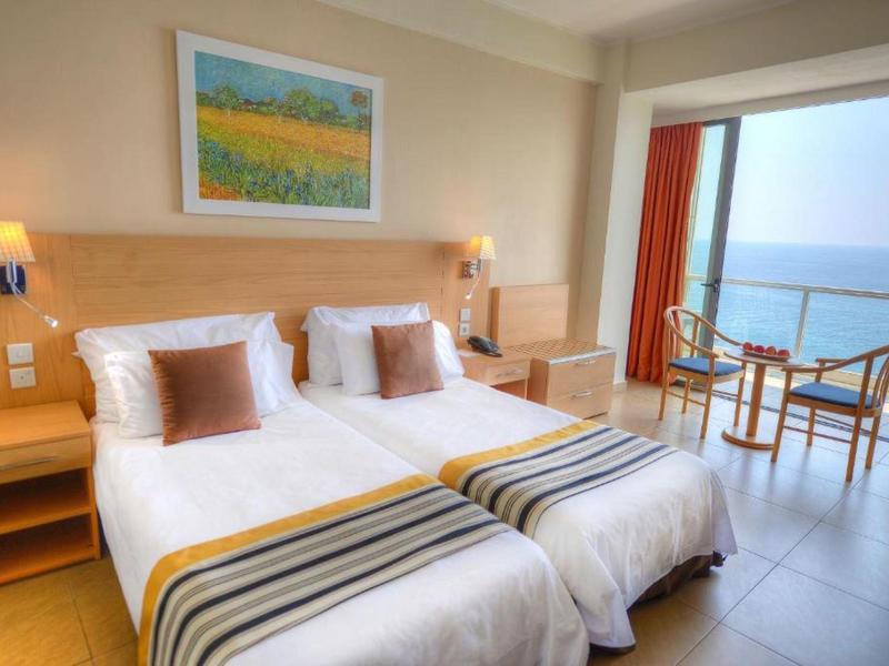 Helles Hotelzimmer mit zwei Einzelbetten, Balkon und Meerblick.