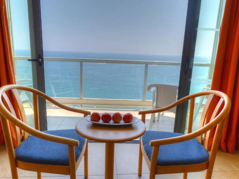 Blick auf Balkon mit zwei Stühlen und einem kleinen Tisch mit Äpfeln, Meer im Hintergrund.