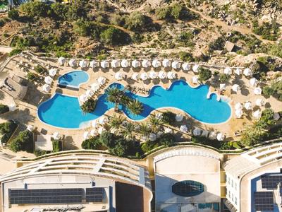 Luftaufnahme eines Resorts mit einem großen, geschwungenen Pool und Sonnenliegen im Freien.