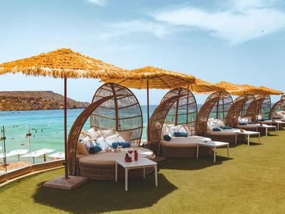 Rund geformte Sonnenliegen mit Strohdächern am Strand mit Meerblick und Menschen im Wasser.