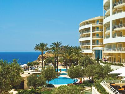 Hotelgebäude mit Rundbalkonen, Palmen und Pool in tropischer Umgebung am Meer.