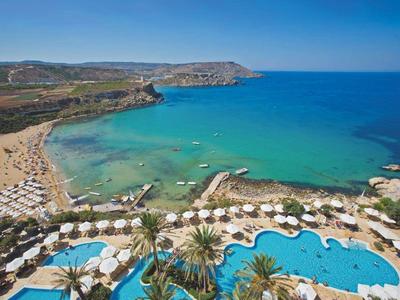 Bahía de playa con mar turquesa, sombrillas y piscina en un complejo hotelero.