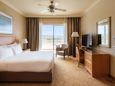 Habitación de hotel luminosa con cama grande, televisión, silla y vista a la terraza.