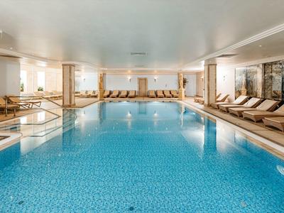 Piscina interior con tumbonas y grandes ventanas en una zona de bienestar luminosa.