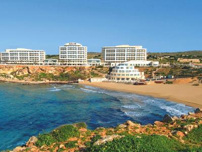 Complejo hotelero con varios edificios junto a una bahía de arena y agua azul clara bajo un cielo despejado.
