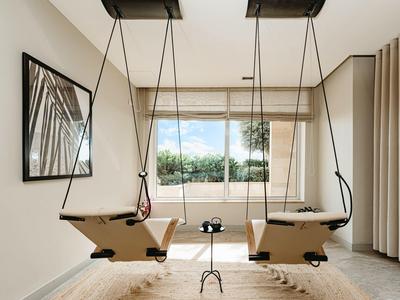 Una habitación luminosa con dos columpios de madera frente a una gran ventana y una alfombra debajo.