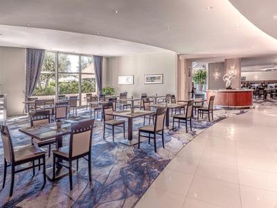 Comedor moderno con mesas de madera, sillas tapizadas y grandes ventanas con vista al verde.