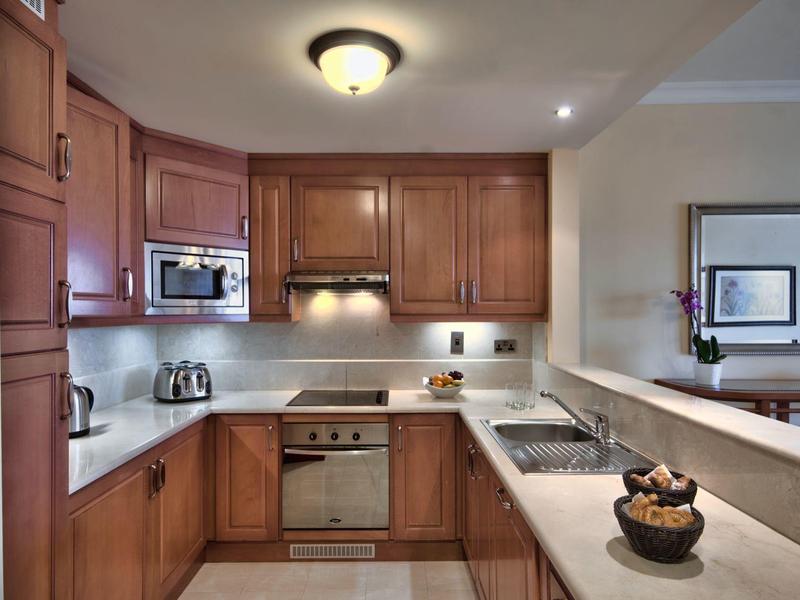 Cocina moderna con gabinetes de madera, electrodomésticos de acero inoxidable y encimera clara en un apartamento de hotel.
