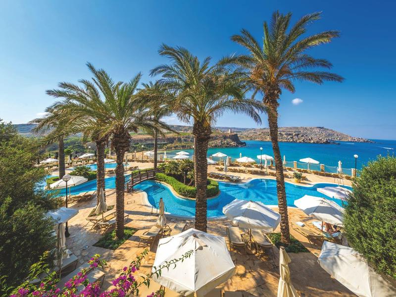 Piscina del hotel con palmeras y vista al mar bajo un cielo azul despejado.