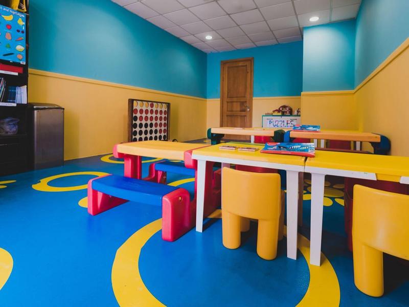 Área de juegos infantil colorida con mesas, sillas pequeñas y juguetes en un interior.