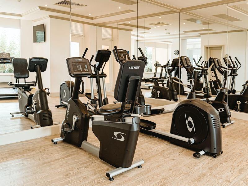 Gimnasio luminoso con varias máquinas de cardio frente a grandes espejos.