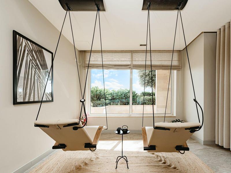 Una habitación luminosa con dos columpios de madera frente a una gran ventana y una alfombra debajo.