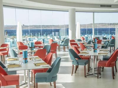 Modernes Restaurant mit bunten Stühlen und Blick auf das Meer durch große Fenster.