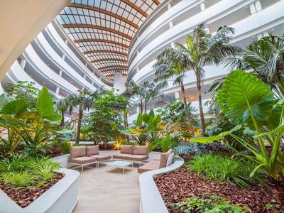 Großer, überdachter Innenhof eines Hotels mit tropischen Pflanzen und Sitzbereichen.