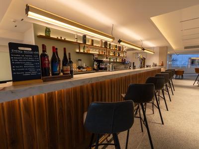 Moderner Hotelbarbereich mit Holztheke und schwarzen Barhockern, beleuchtet und gemütlich.