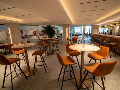 Moderne Hotelbar mit braunen Ledersesseln, hohen Tischen und gedämpfter Beleuchtung.