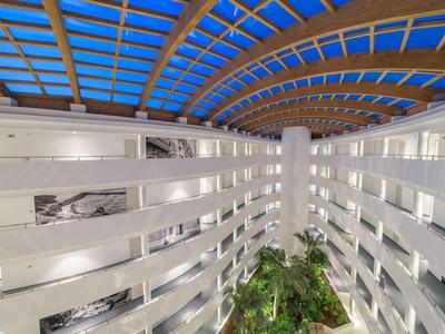 Innenansicht eines modernen Hotels mit einer Glasdecke und grünen Pflanzen im Atrium.