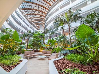 Moderner Hotelinnenhof mit tropischen Pflanzen und Sitzbereichen unter einem Glasdach.