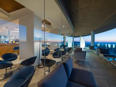 Moderner Hotelbereich mit Glaswand, Sitzgruppen und Meerblick bei Dämmerung.