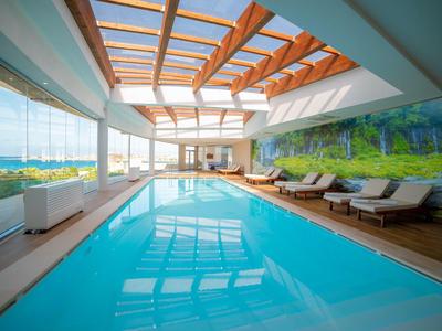 Hallenbad mit großen Fenstern, Holzdecke und Liegestühlen neben dem Pool.