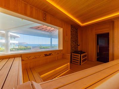Holzsauna mit großer Fensterfront und Blick auf Wasser und Berge bei Sonnenlicht