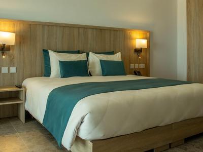 Modern eingerichtetes Hotelzimmer mit großem Bett, zwei Nachttischen und hölzerner Wandverkleidung.