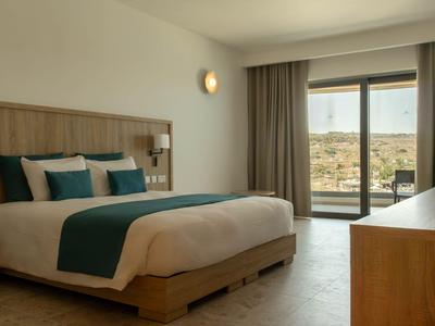Modernes Hotelzimmer mit großem Bett, Holzmöbeln und Panoramafenster mit Blick auf die Landschaft.
