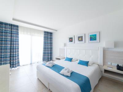 Modernes Hotelzimmer mit Doppelbett, weißen und blauen Akzenten und großen Fenstern mit Vorhängen.