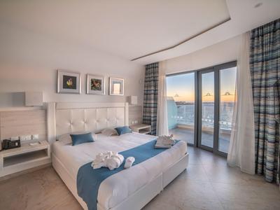 Modernes Hotelzimmer mit großem Bett, Panoramafenstern und Blick auf den Sonnenuntergang.