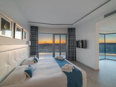 Modern eingerichtetes Hotelzimmer mit Doppelbett und Meerblick bei Sonnenuntergang.