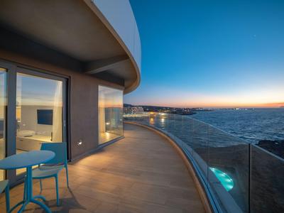 Moderne Hotelterrasse mit Glasgeländer und Blick auf das Meer bei Sonnenuntergang.