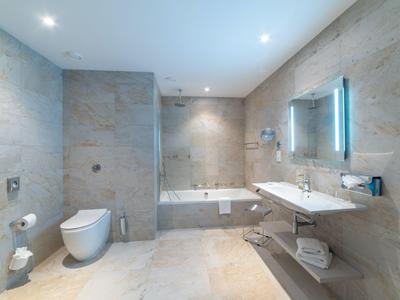 Modernes Badezimmer mit Badewanne, Toilette und großem beleuchtetem Spiegel.